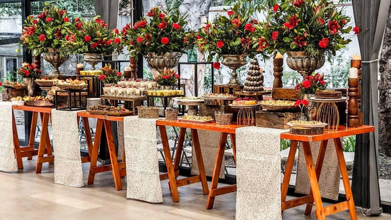 Buffet en mesones de madera con centros de flores rojas